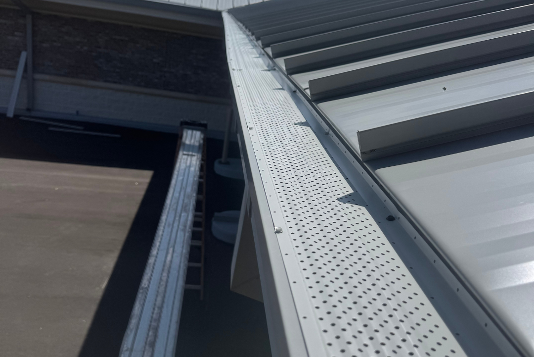 Aluminum gutter guard installed along metal roof to prevent debris buildup